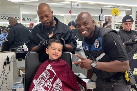 Police officer next to barber giving child a free haircut